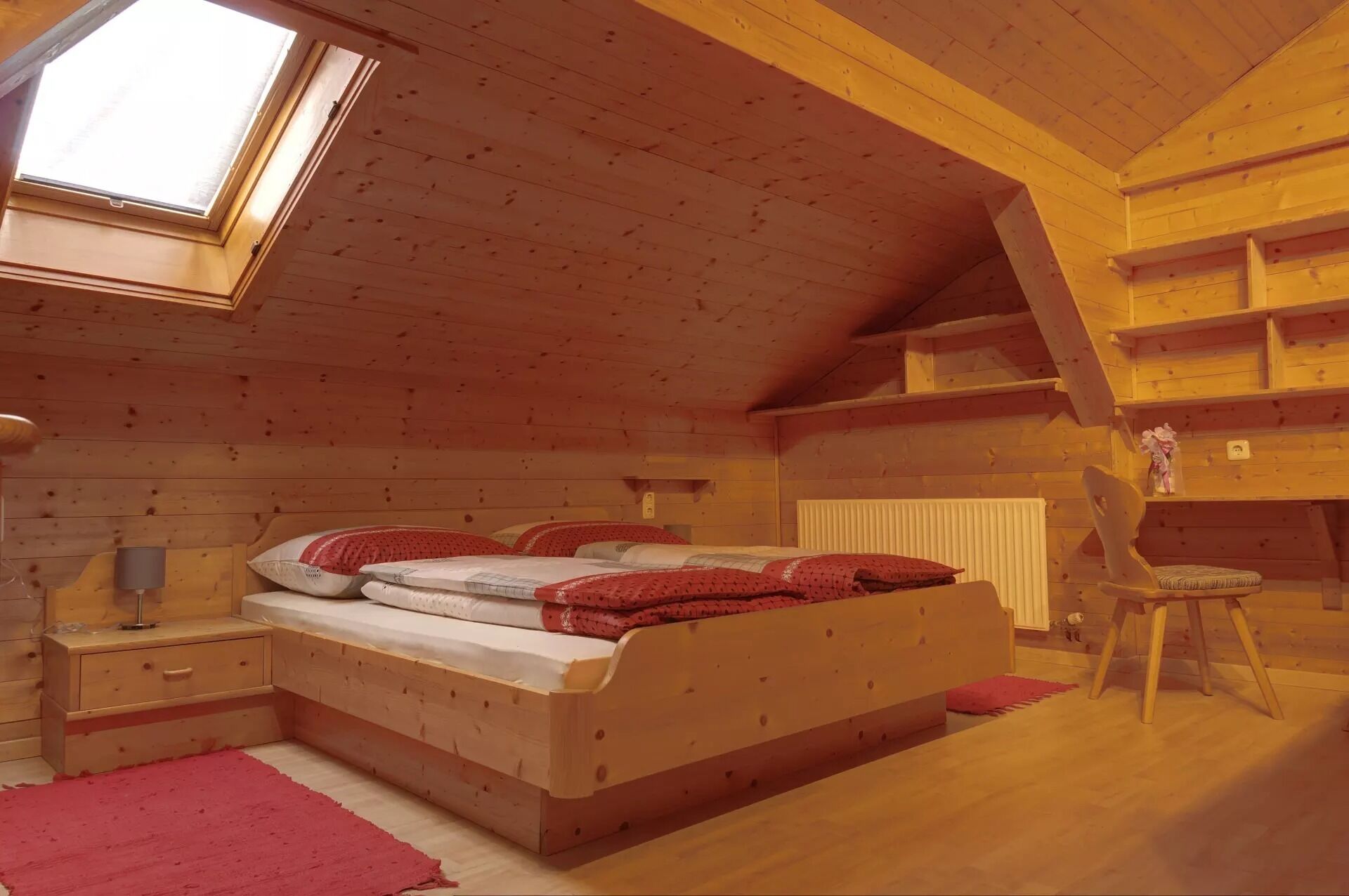 A cozy attic bedroom with a skylight, a wooden bed, a nightstand, a chair, and a radiator.