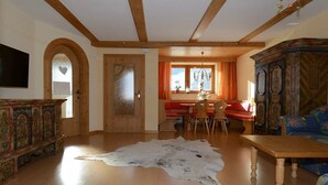 Ein geräumiges Wohnzimmer mit Holzbalken, einem großen Fellteppich, einer Holzkommode und einem traditionellen Sofa.