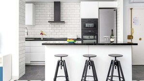 Cocina moderna con armarios blancos, encimera negra y tres taburetes negros.
