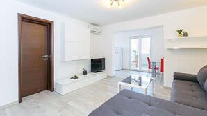 A modern living room with a grey sofa, a flat-screen TV, and a glass coffee table. - Apartment Janko (Medulin)