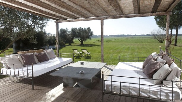 Terraza exterior con dos camas y una mesa, con vistas a un campo de césped.
