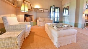 Una sala de estar acogedora con un sillón a rayas, un sofá color beige y un pequeño reposapiés con adornos.