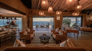 A spacious living area with a view of the ocean, furnished with sofas and a coffee table, and a dining area with tables and chairs.