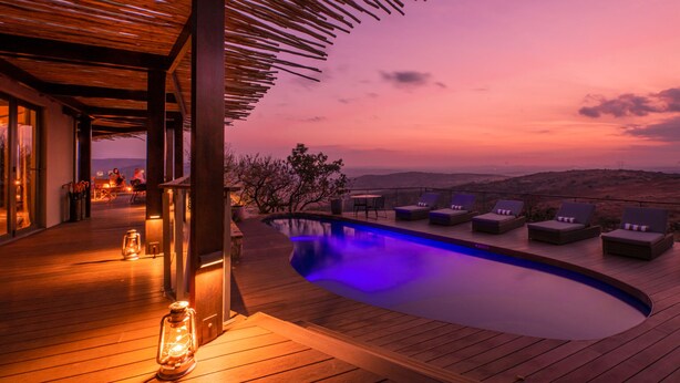 A wooden deck with a pool, lounge chairs, and a view of the landscape.