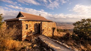 A stone building with a tiled roof, a stone staircase leading to a door, and a view of the countryside.