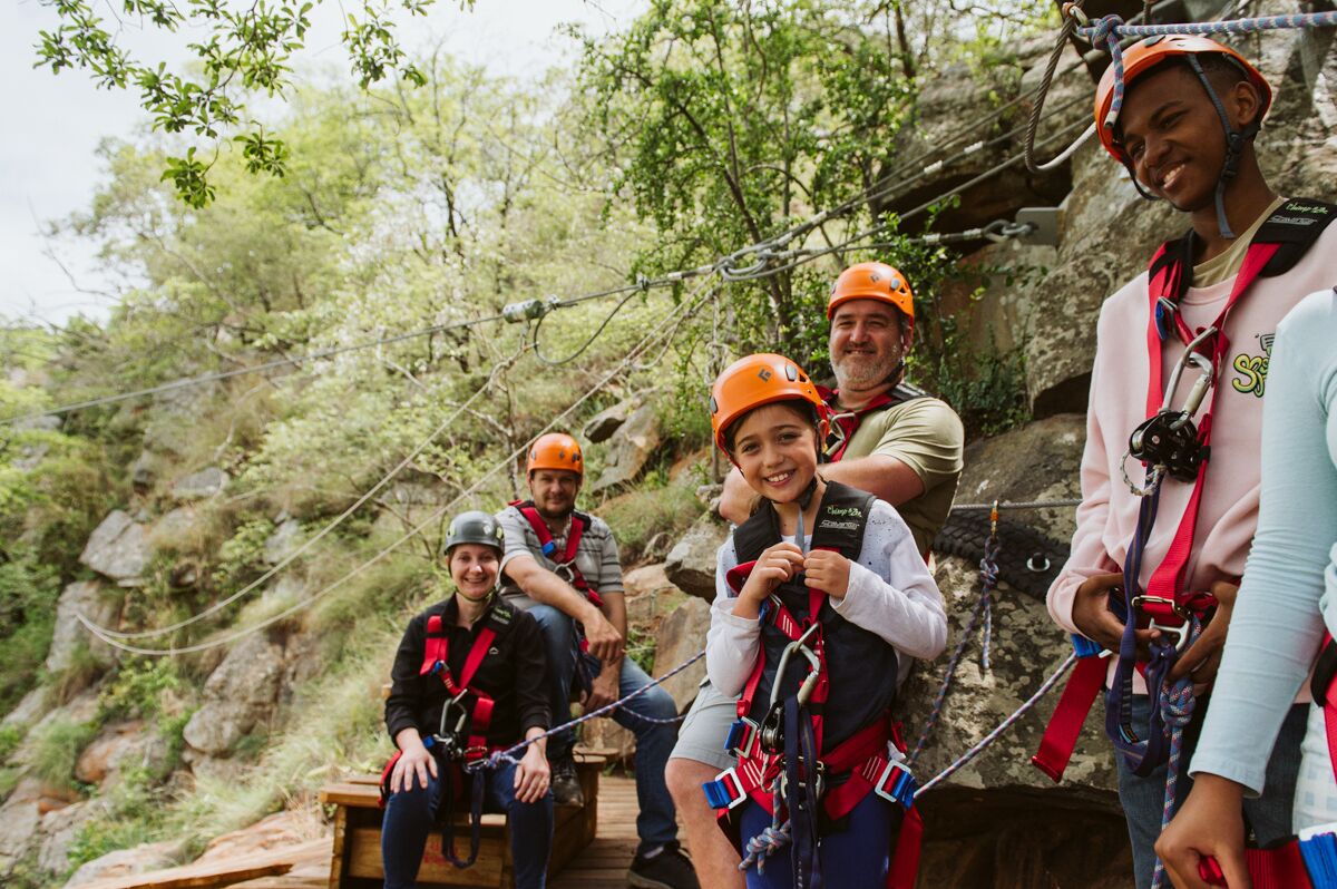Un grupo de personas con cascos y arneses, sentadas sobre una plataforma de madera al aire libre.