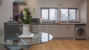 A modern kitchen with a glass dining table, a built-in oven, and a washing machine. - HEREFORDSHIRE – Little Oak: Charming Rural Cottage, Sleeps 2, Cozy Getaway (HEREFORD)