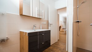 A modern bathroom with a wooden vanity, a white sink, and a shower area. - Haus Seeweg Geierswalde - Apartment 2 (Elsterheide)