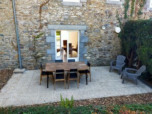 A stone building with a wooden table and chairs in a courtyard. - Gite Essentiel (Gratot)