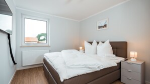 Un dormitorio con cama, mesitas de noche, una ventana y un radiador.