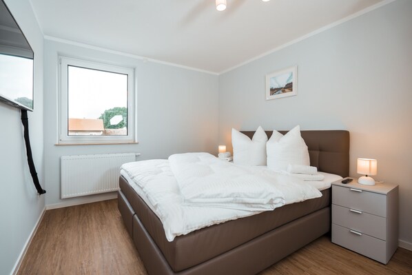 Une chambre à coucher avec un lit, des tables de chevet, une fenêtre et un radiateur.
