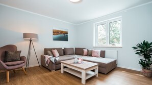Una sala de estar moderna con sofá, sillón, mesa de centro, lámpara de pie y ventana con vista a árboles.