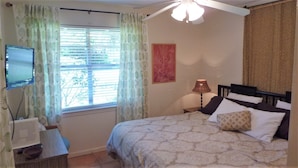 A bedroom with a bed, a desk with a computer, a lamp, and a window with curtains.