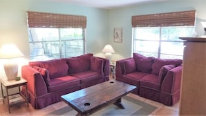A living room with two purple sofas, a wooden coffee table, a lamp, and a window with a view of a fence.