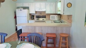 A compact kitchen with white cabinets, a central island with stools, a microwave, and a stove.