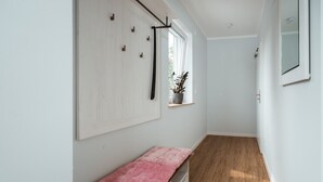 Un pasillo estrecho con un banco, una ventana con una planta y una puerta.