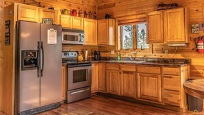 Una cocina tipo cabaña con armarios de madera, un refrigerador de acero inoxidable, un microondas y una estufa.