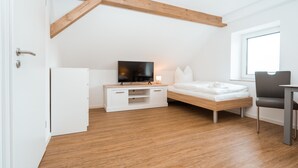 Un dormitorio pequeño y moderno con techo de madera, una cama, un televisor sobre un tocador blanco y una ventana.