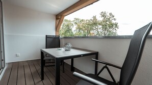 Un balcón con una mesa, una silla, una lámpara de mesa pequeña y vistas a árboles.