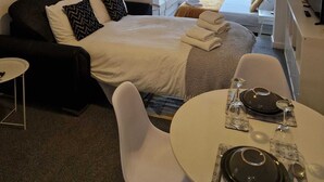 Una habitación de hotel moderna con una cama grande, un escritorio y una zona de comedor. Hay tres cuadros en la pared y una decoración con cabeza de venado.