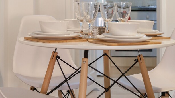 Comedor con una mesa redonda dispuesta para cuatro personas, sillas blancas y vista a un edificio a través de una ventana.