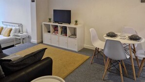 Una sala de estar moderna con un sofá, una mesa de comedor con sillas, un televisor sobre un mueble blanco y obras de arte en la pared.