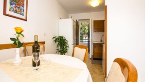 A dining area with a table set for two, a bottle of wine, and a vase with a yellow rose. There is a potted plant and a chair visible. - Beautiful view apartment Loreta (Labin)