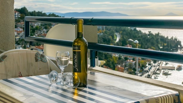A table with a bottle of wine, a glass, and a chair with a view of a coastal landscape. - Beautiful view apartment Loreta (Labin)