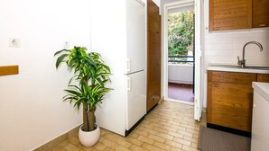 A compact kitchen with a white refrigerator, wooden cabinets, a potted plant, and a view through an open door to an outdoor balcony. - Beautiful view apartment Loreta (Labin)