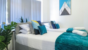 Een hotelkamer met twee bedden, een groot raam met jaloezieën, een schilderij aan de muur en een kamerplant.