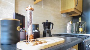 Een aanrecht met een koffiezetapparaat, een pepermolen, een snijplank en een fles wijn.