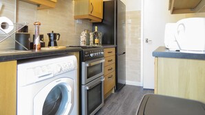 Een kleine keuken met houten kastjes, een roestvrijstalen fornuis, een inbouwoven, een koelkast en een wasmachine.