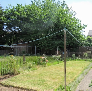 Stroll through the serene garden, surrounded by a variety of plants and flowers, including roses, along a paved path.