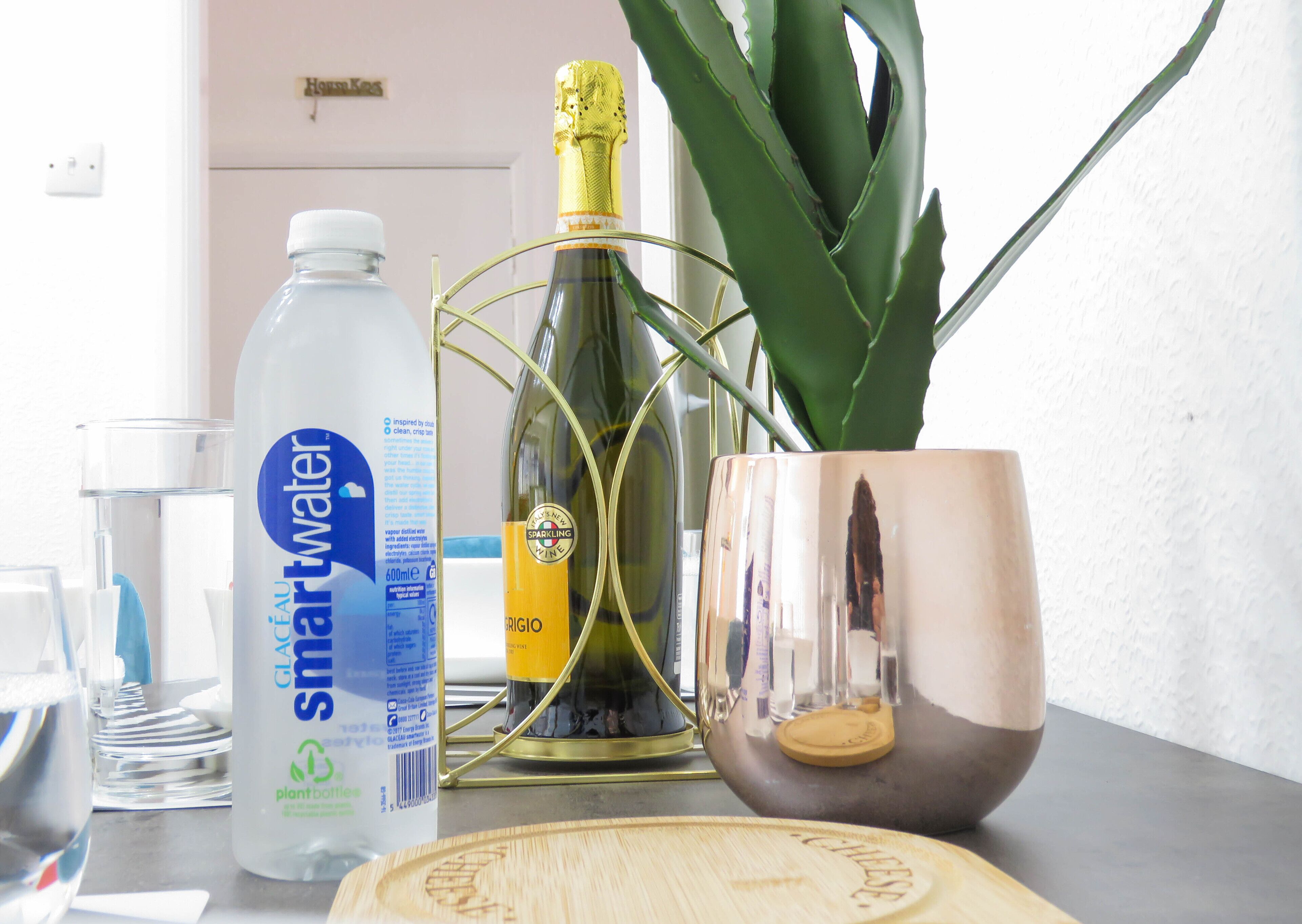 A table with a bottle of Smartwater, a bottle of sparkling wine, a glass, a plant, and a decorative bowl.
