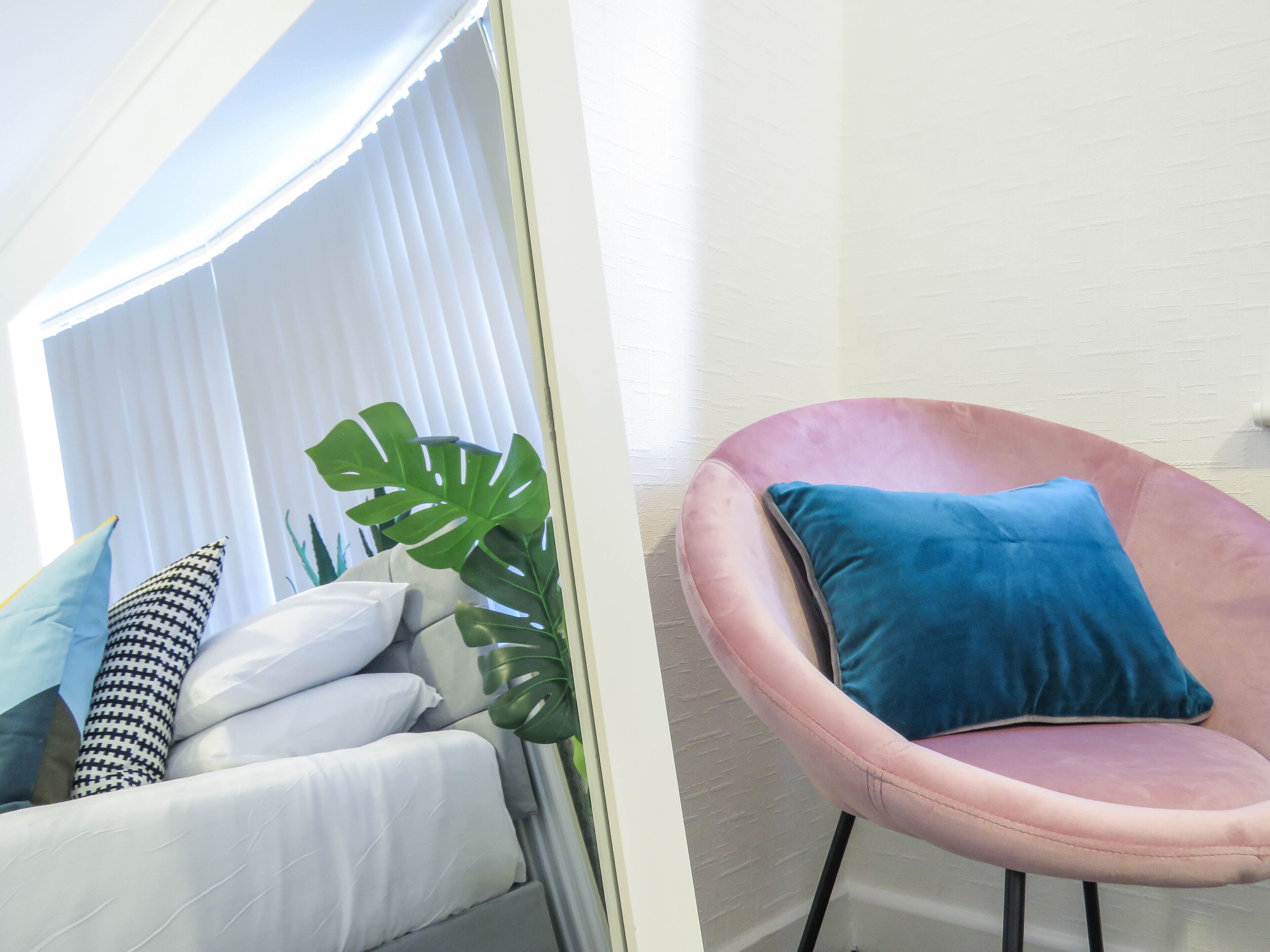 A room with a white sofa set, a pink chair with a blue cushion, and a large green plant.