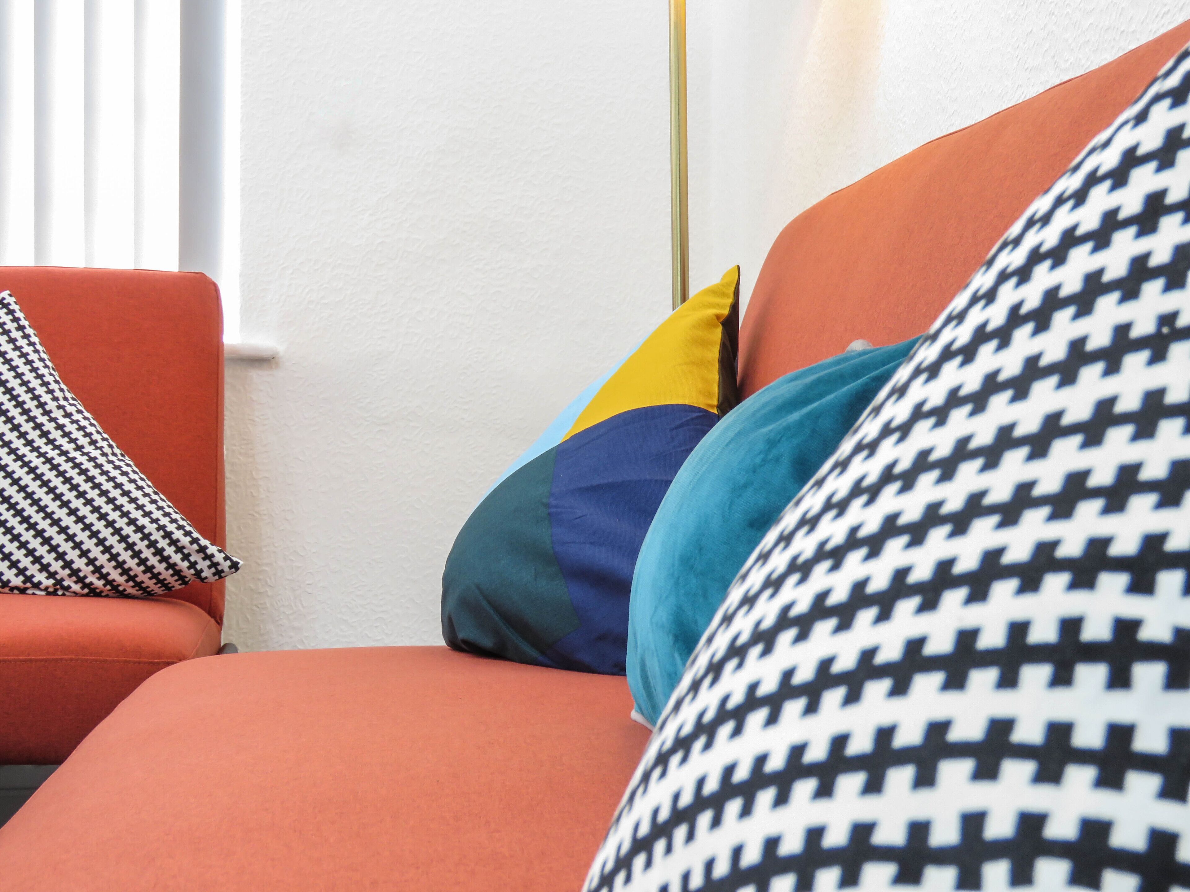 A modern living room with a sofa and multiple cushions in various colors and patterns.
