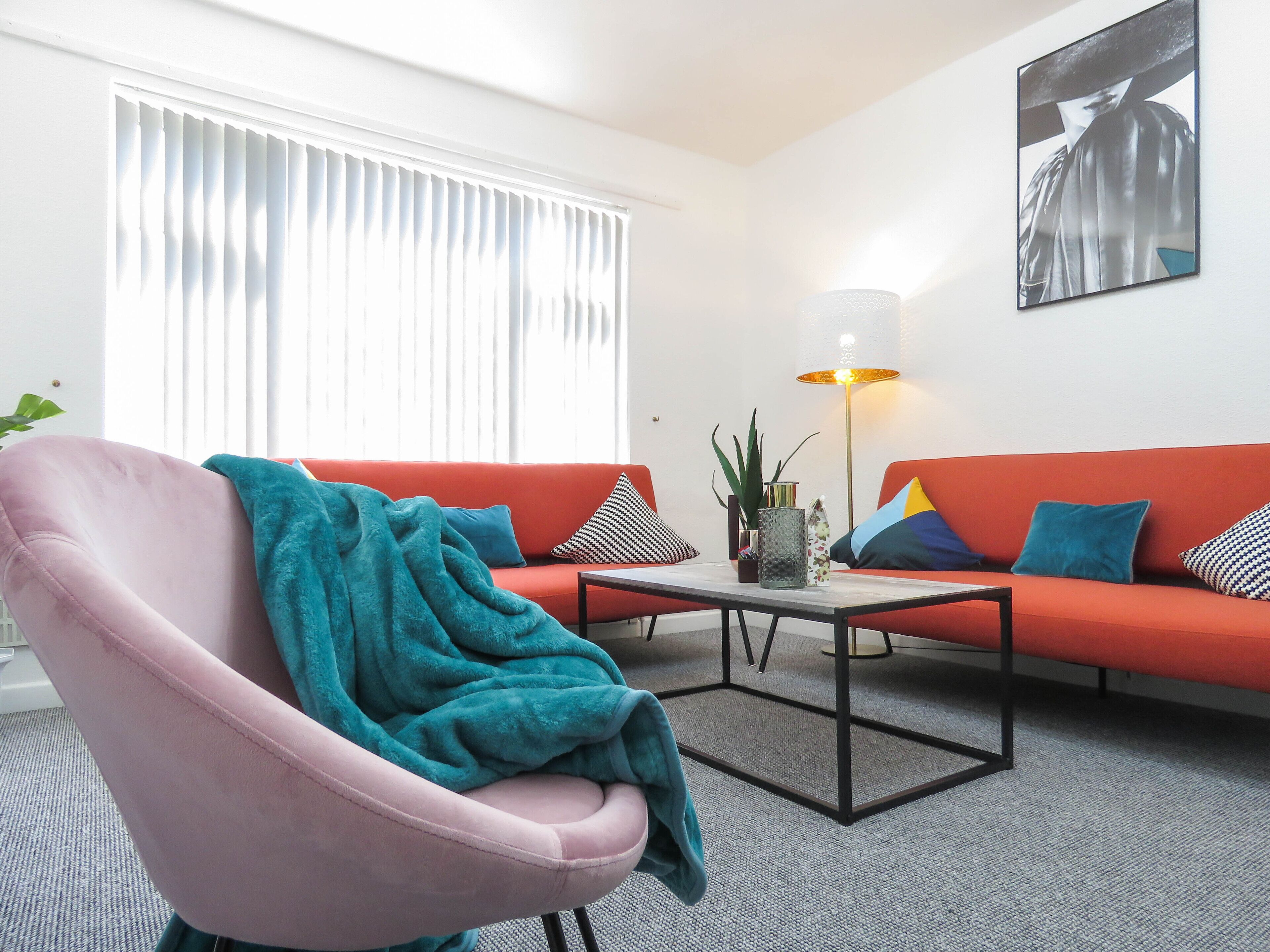 Een moderne woonkamer met een roze fauteuil, een rode bank en een salontafel.