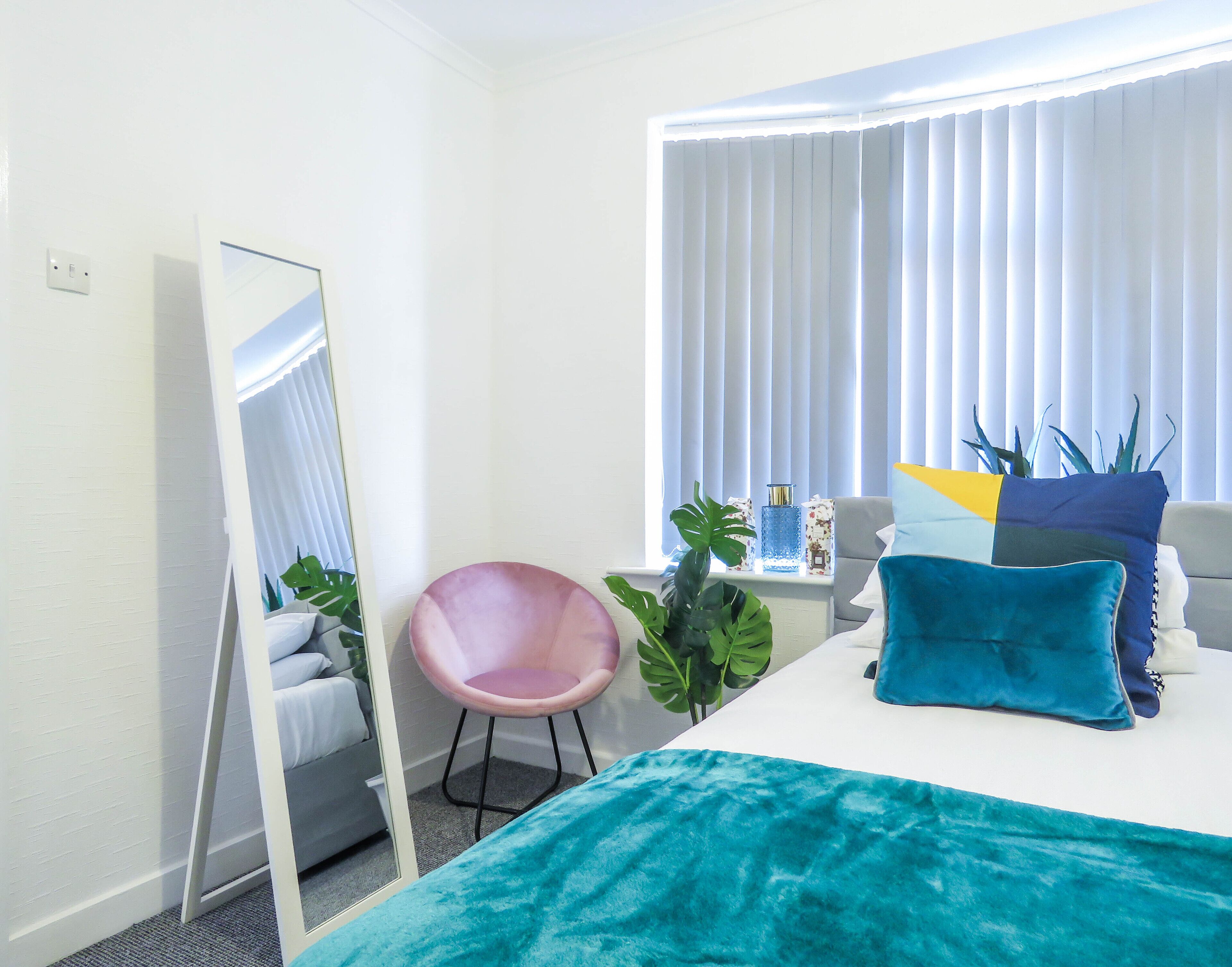 Une chambre d’hôtel avec un lit, une chaise, un bureau, un miroir et une fenêtre avec des rideaux.