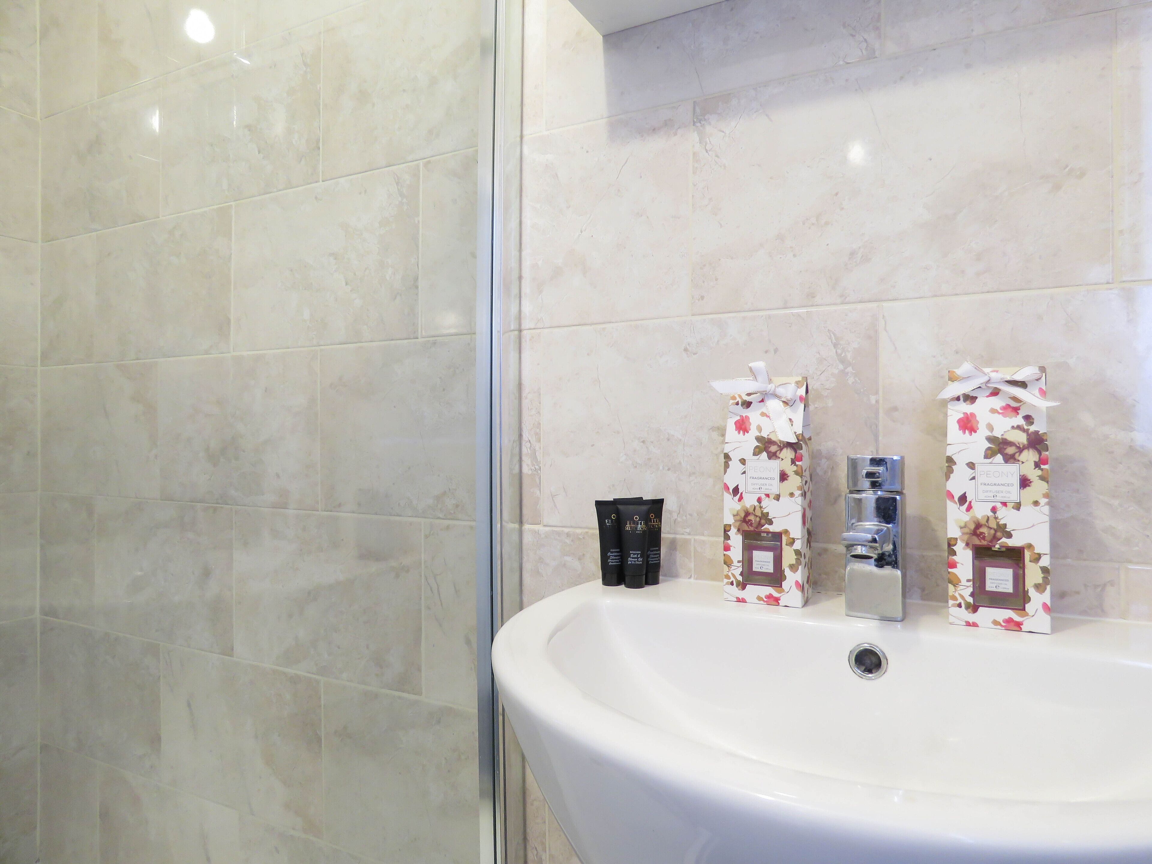 A bathroom with a white sink, two toiletries, and a shower area with beige tiles.