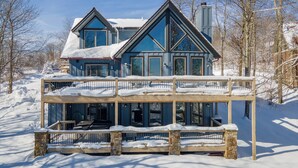 Ein großes, zweistöckiges Haus mit Balkon und Natursteinfassade, umgeben von Schnee und Bäumen.