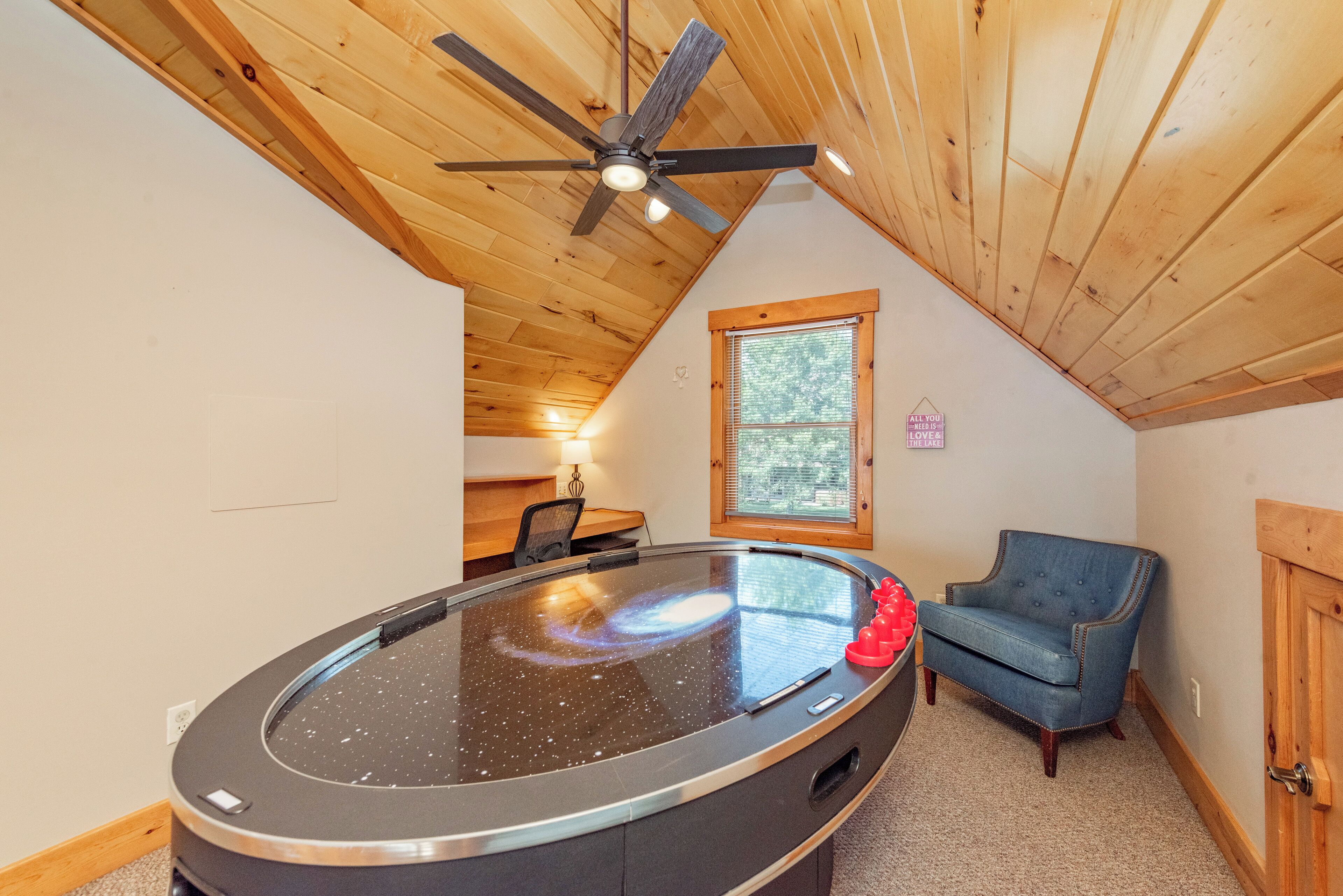 A room with a ceiling fan, a round table with a glass top, a blue armchair, and a window with blinds.