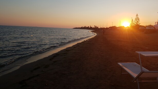 Una playa al atardecer con cielo despejado, mar tranquilo y una fila de sillas de playa.