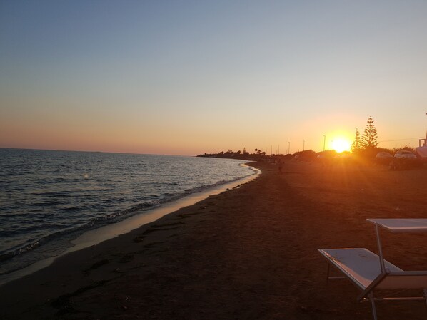 A beach at sunset with a clear sky, calm sea, and a row of beach chairs.