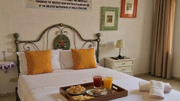 A neatly made bed with a tray of breakfast items, including cereal, fruit, and juice, in a hotel room. - 6 Keys (Pisa)