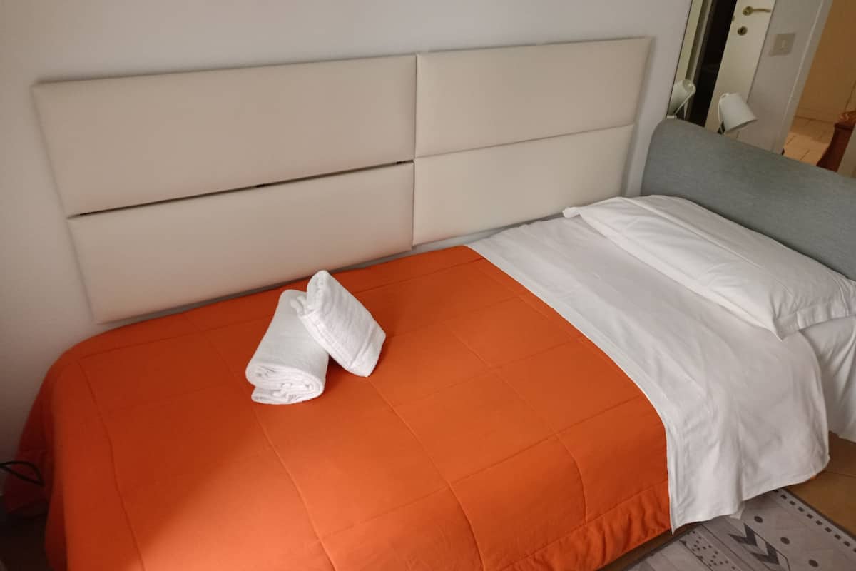Una cama bien hecha con colcha naranja y almohadas blancas, cabecera blanca y pie de cama gris.
