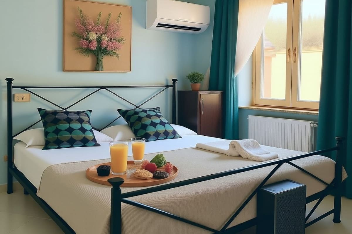 Una cama bien hecha con una bandeja de desayuno, una mesita de noche, un radiador y una ventana con cortinas.