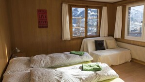 A room with two beds, a sofa, and large windows with a view of mountains. - Guesthouse Alive (Adelboden)