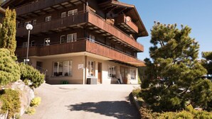 A multi-story wooden building with balconies, a covered entrance, and a paved driveway. - Guesthouse Alive (Adelboden)