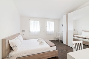 A modern bedroom with a wooden bed, white linens, a bedside table, a chair, and a wardrobe.