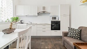 A compact kitchen with white cabinets, a microwave, and an oven. There's a dining table with chairs and a potted plant.
